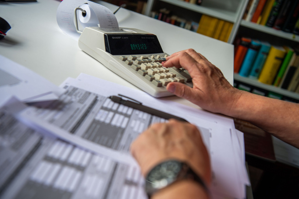 Ein Steuerzahler füllt seine Steuererklärung aus und tippt zur Berechnung Zahlen in einen Tischrechne