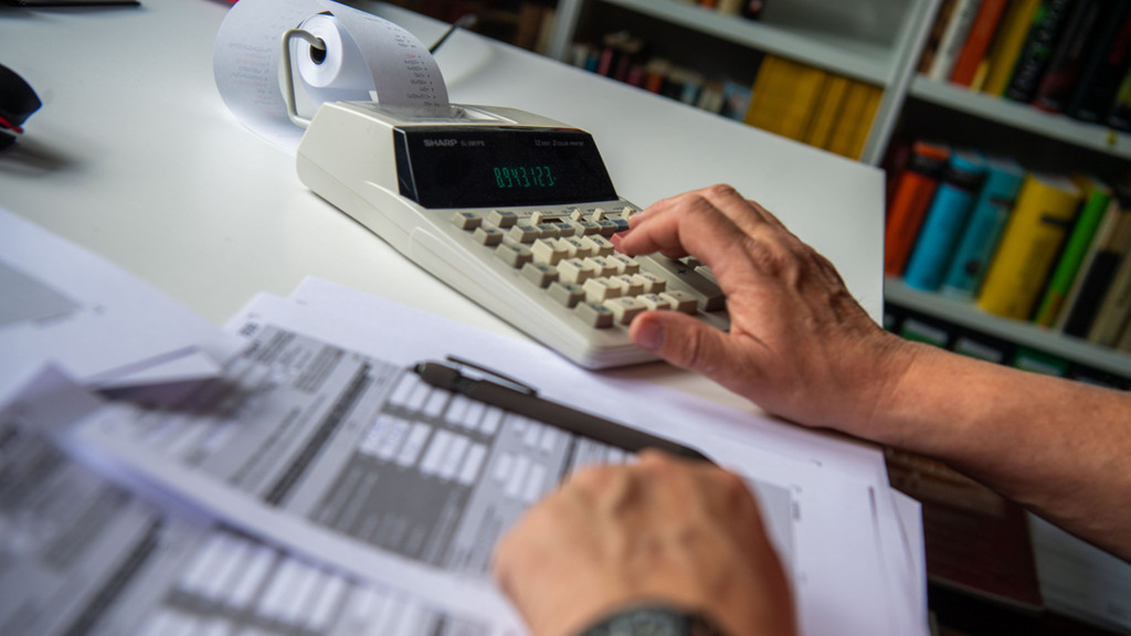 Ein Steuerzahler füllt seine Steuererklärung aus und tippt zur Berechnung Zahlen in einen Tischrechne