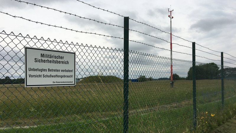 An einem hohen Zaun hängt ein Warnschild, darauf steht: "Militärischer Sicherheitsbereich. Unbefugtes Betreten verboten! Vorsicht Schußwaffengebrauch!" | Bild: BR/Susanne Pfaller An einem hohen Zaun hängt ein Warnschild, darauf steht: "Militärischer Sicherheitsbereich. Unbefugtes Betreten verboten! Vorsicht Schußwaffengebrauch!"