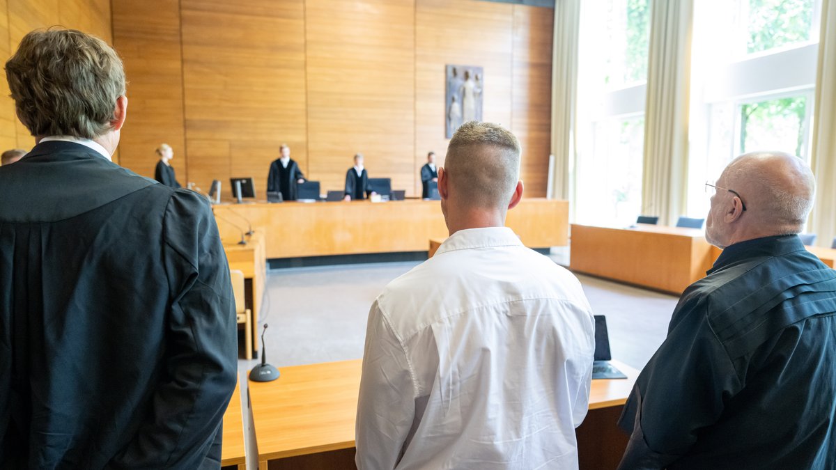 Der Kläger Andreas Perr (M) und seine Anwälte Andreas Schulz (r) und Markus Goldbach (l) stehen zu Prozessbeginn an ihren Plätzen im Gerichtssaal des Landgericht Traunstein. 