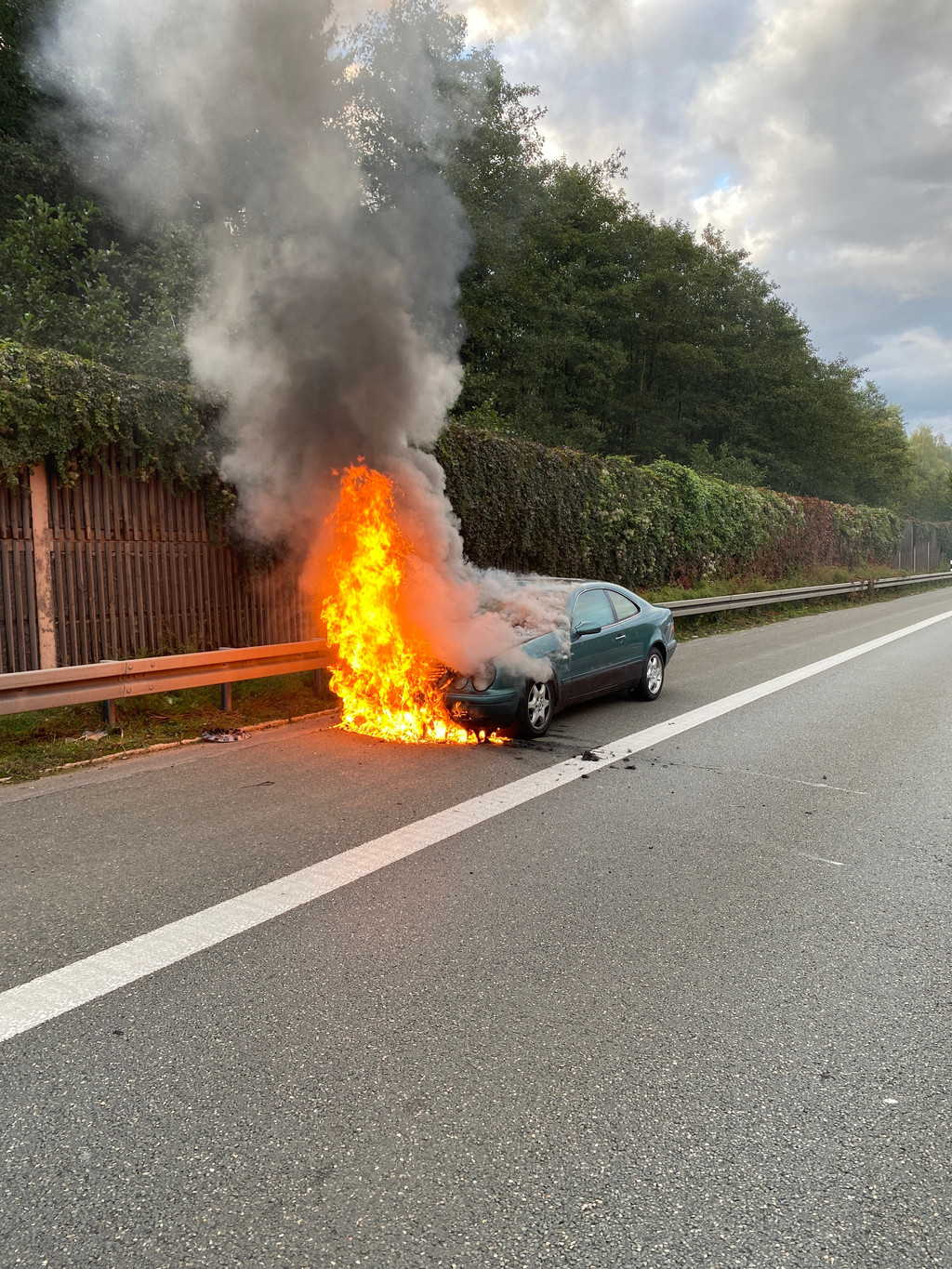 Ein brennendes Auto parkt auf dem Standstreifen einer Autobahn.