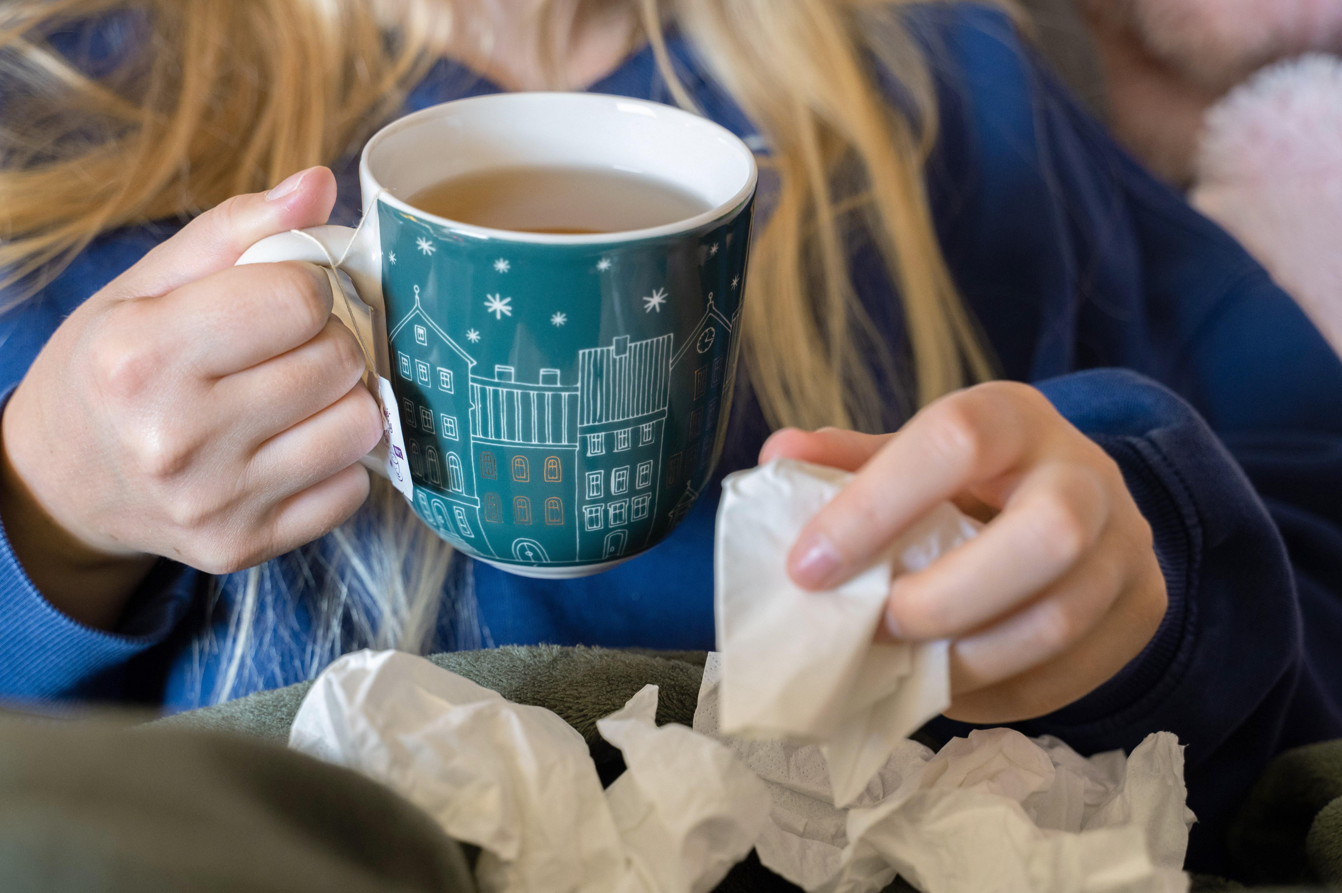 (Symbolbild) Eine Frau hält eine Teetasse und ein Taschentuch in der Hand. 