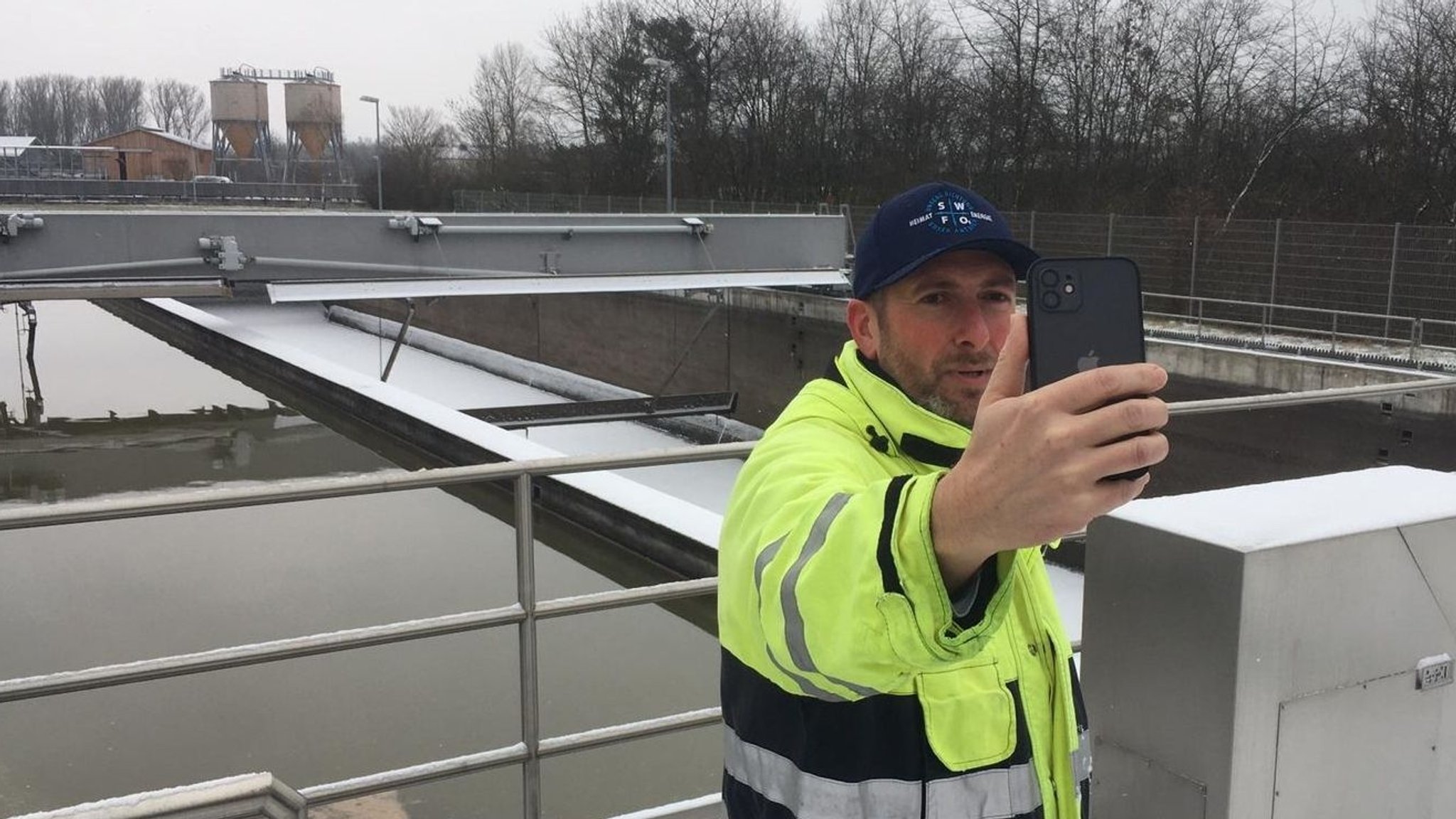 Gernot Reichel steht mit einem Smartphone in einer Kläranlage in Forchheim.