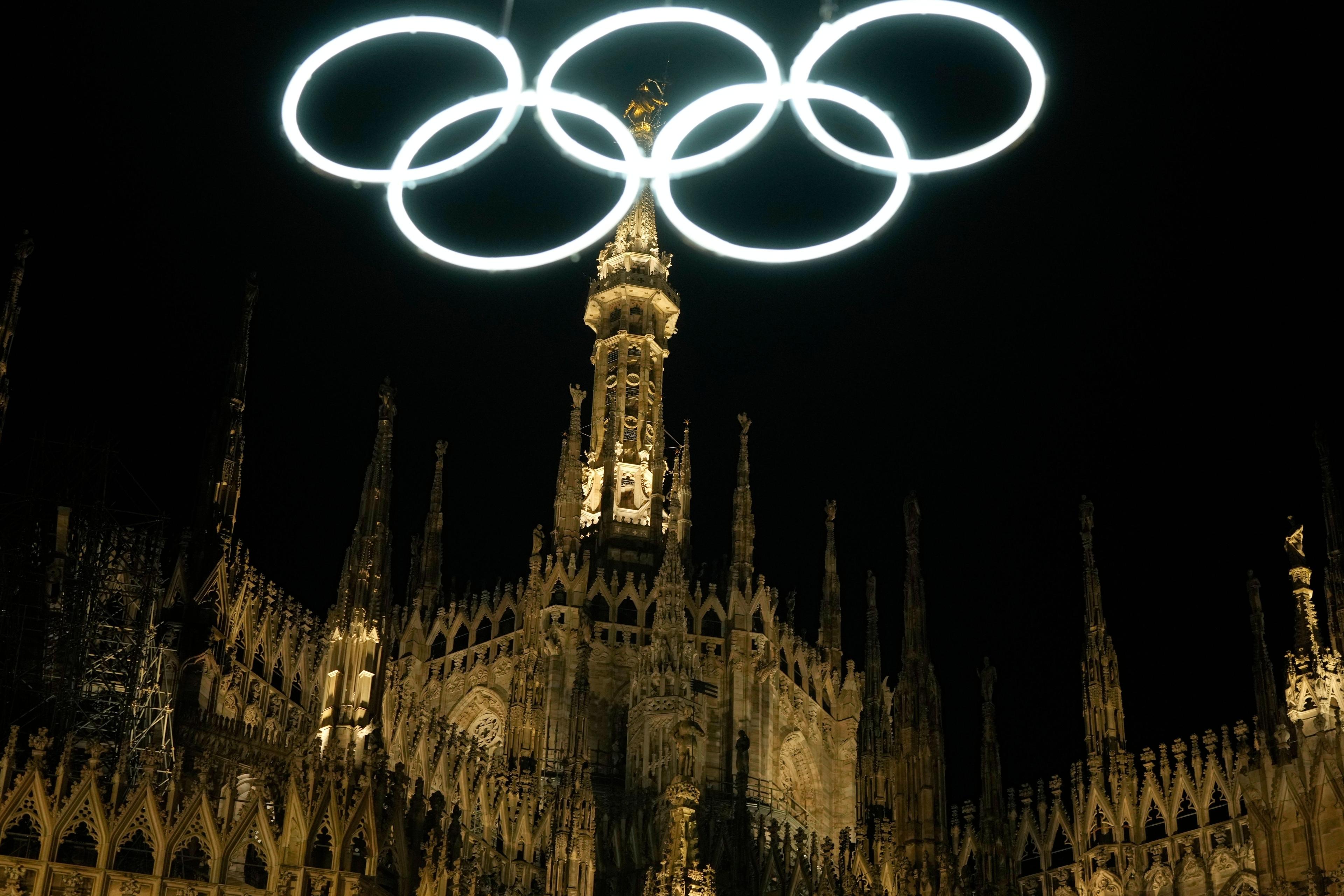 27.12.2025, Italien, Mailand: Olympische Ringe leuchten neben dem gotischen Dom für die bevorstehenden Olympischen Winterspiele in Mailand. Foto: Luca Bruno/AP/dpa +++ dpa-Bildfunk +++