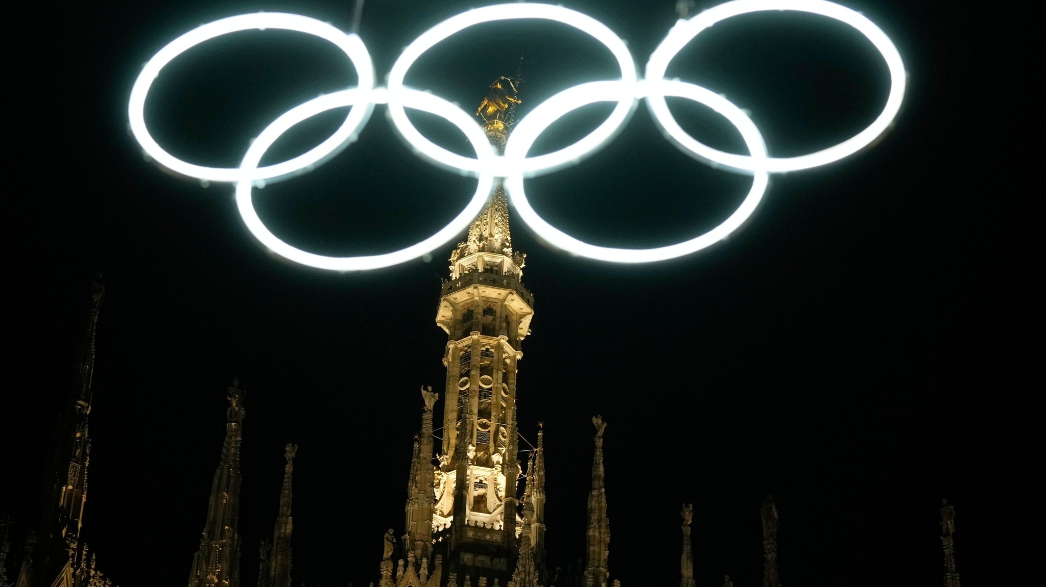 27.12.2025, Italien, Mailand: Olympische Ringe leuchten neben dem gotischen Dom für die bevorstehenden Olympischen Winterspiele in Mailand. Foto: Luca Bruno/AP/dpa +++ dpa-Bildfunk +++