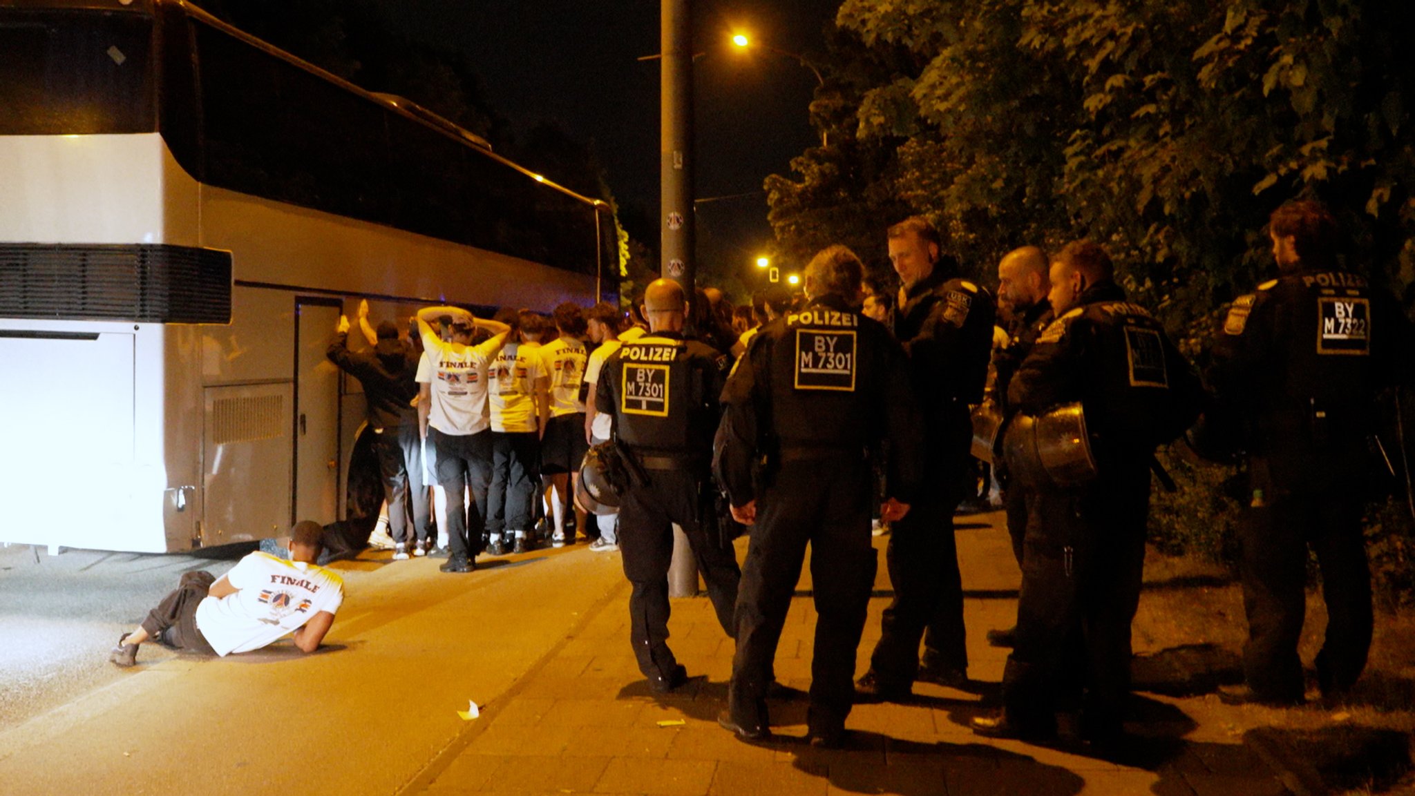 Foto: Nachts stehen Polizisten neben Fans neben einem Reisebus.