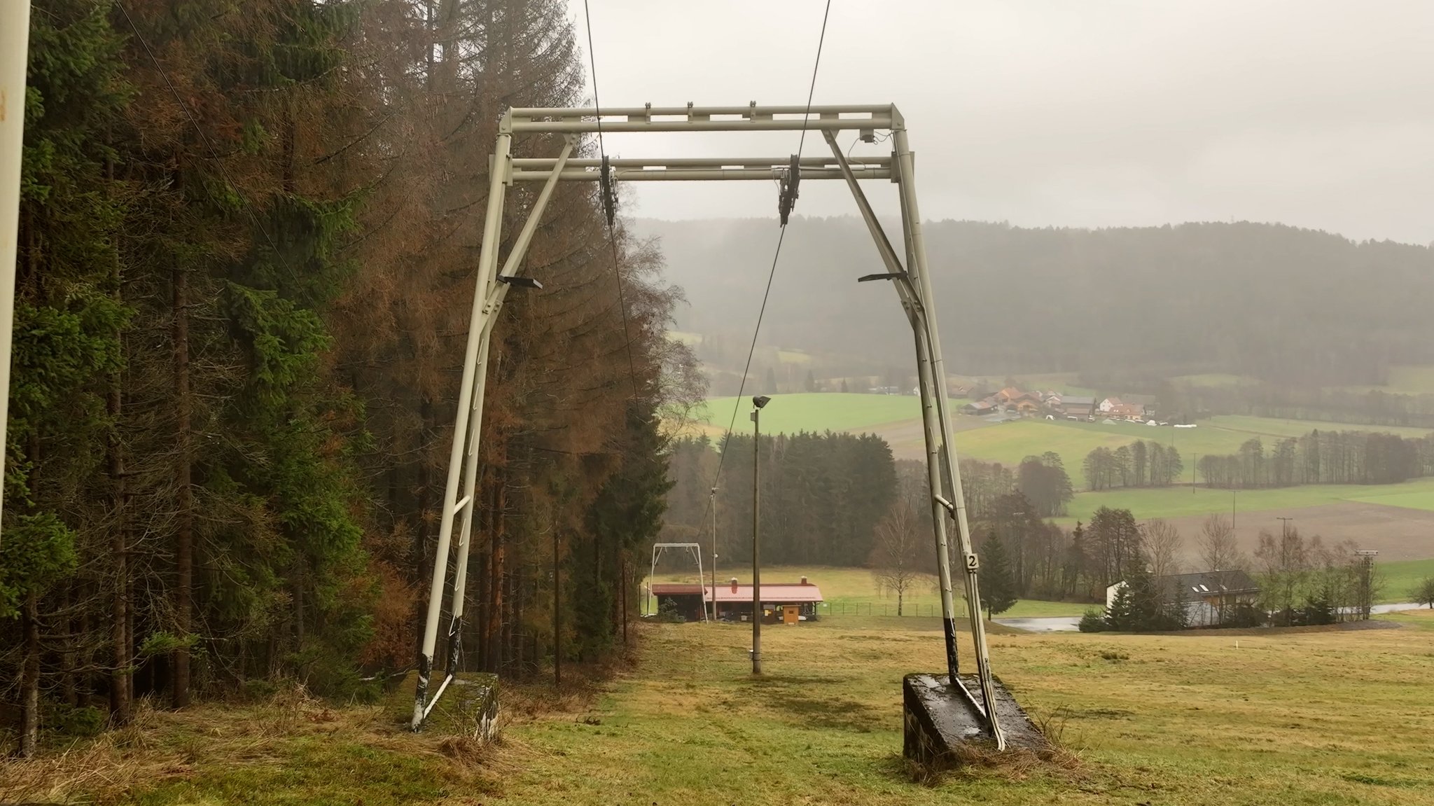 Ein Lift steht auf einer grünen Wiese, im Hintergrund sind Wald, Felder und Bauernhöfe zu sehen. 