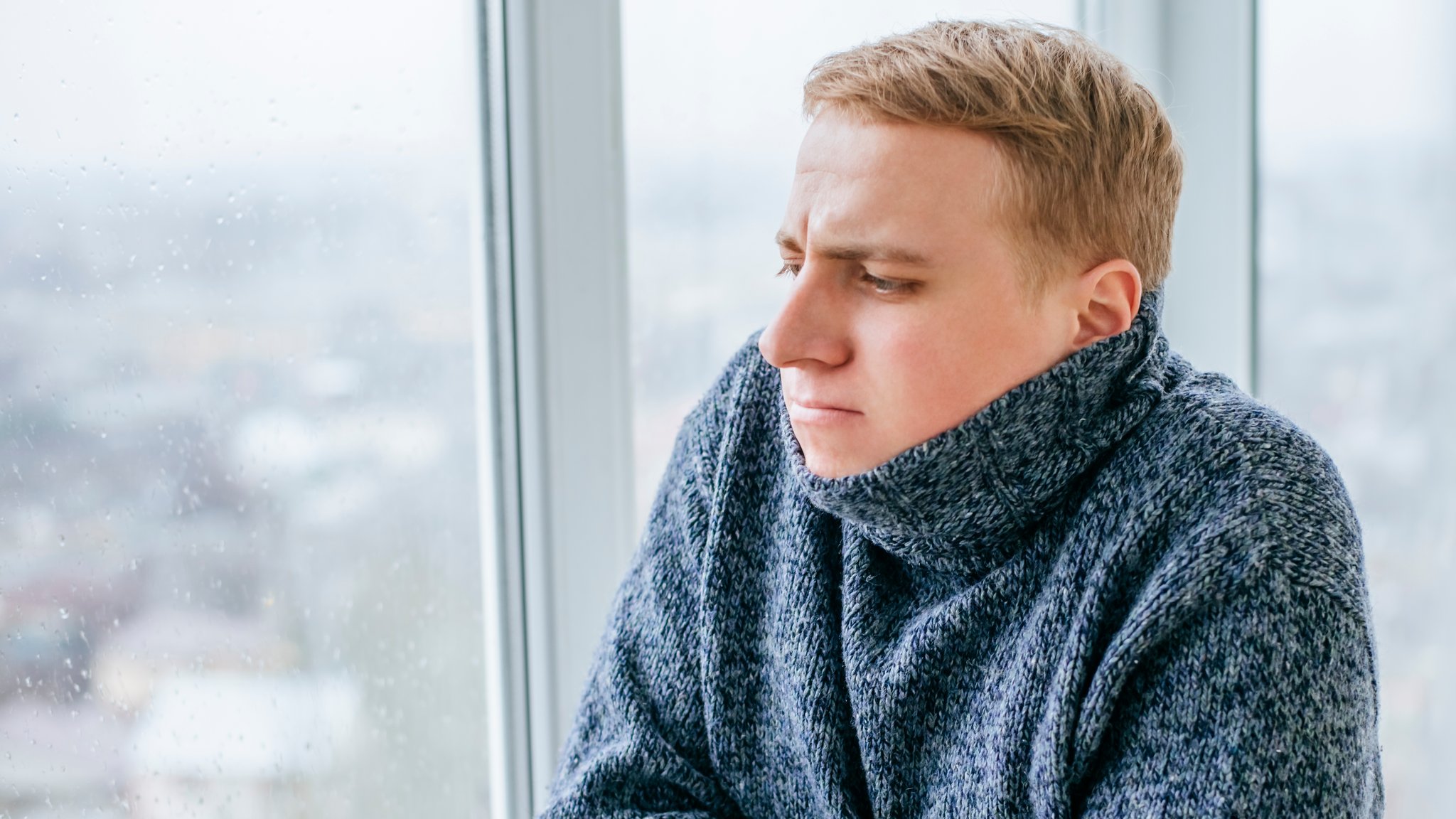 Mann steht am Fenster und fröstelt (Symbolbild)