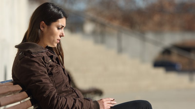 Eine Frau sitzt niedergeschlagen wirkend auf einer Bank im Freien | Bild: colourbox.com Eine Frau sitzt niedergeschlagen wirkend auf einer Bank im Freien