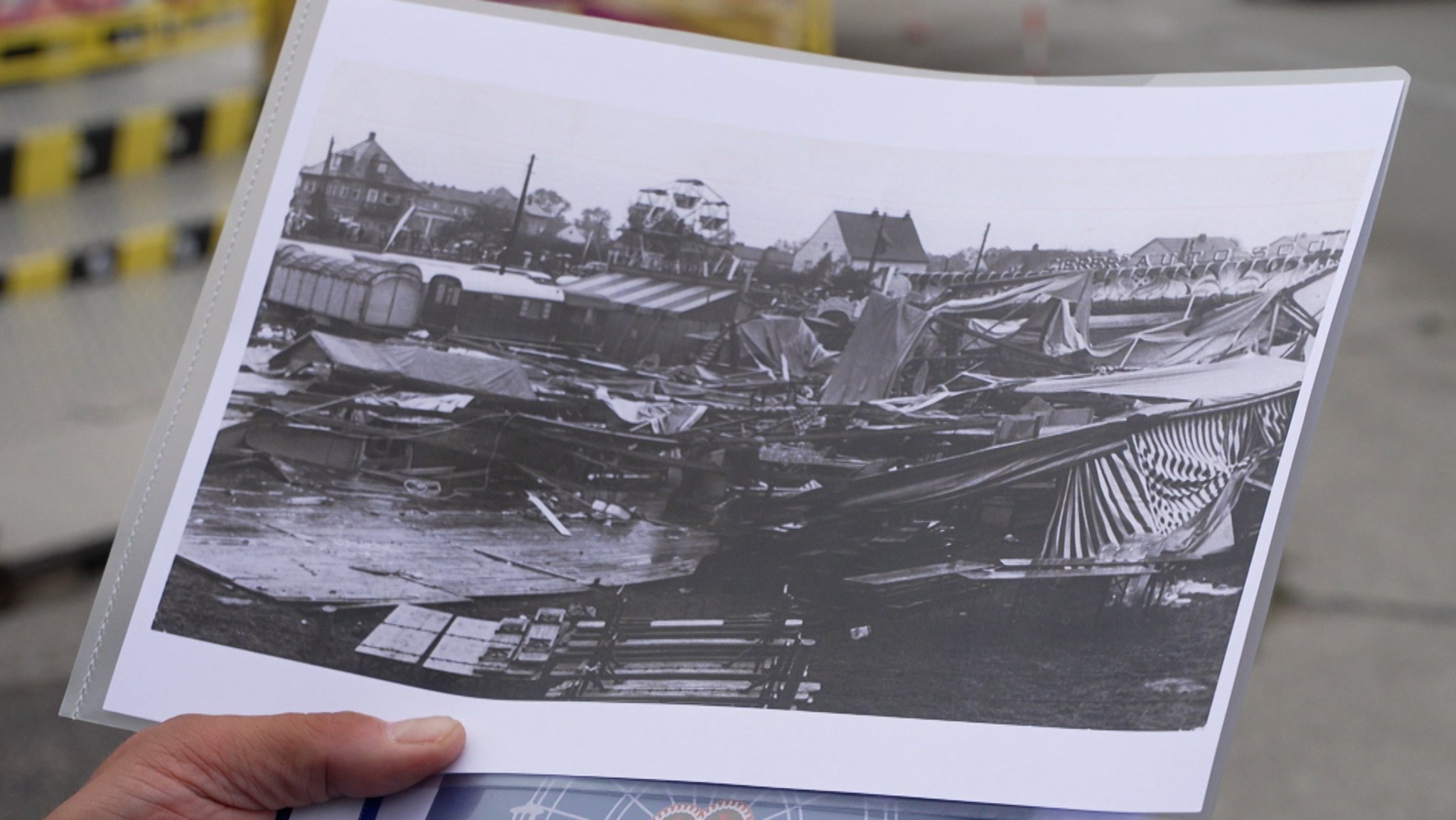 Hand hält Bild (s/w) mit zerstörten Buden und Zelten nach Unwetter