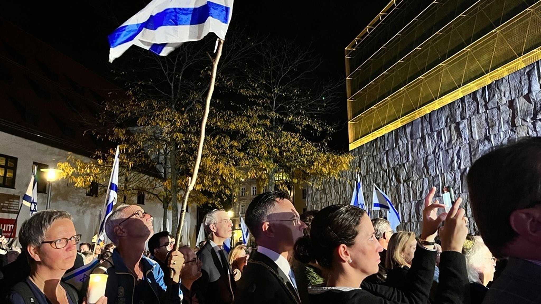 Menschen stehen mit brennenden Kerzen und Israel-Fahnen auf dem Münchner Jakobsplatz.