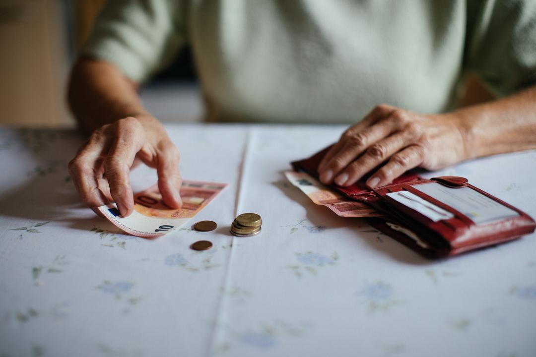 Eine Seniorin hat vor sich auf dem Tisch einen Geldbeutel mit Münzen und Scheinen liegen