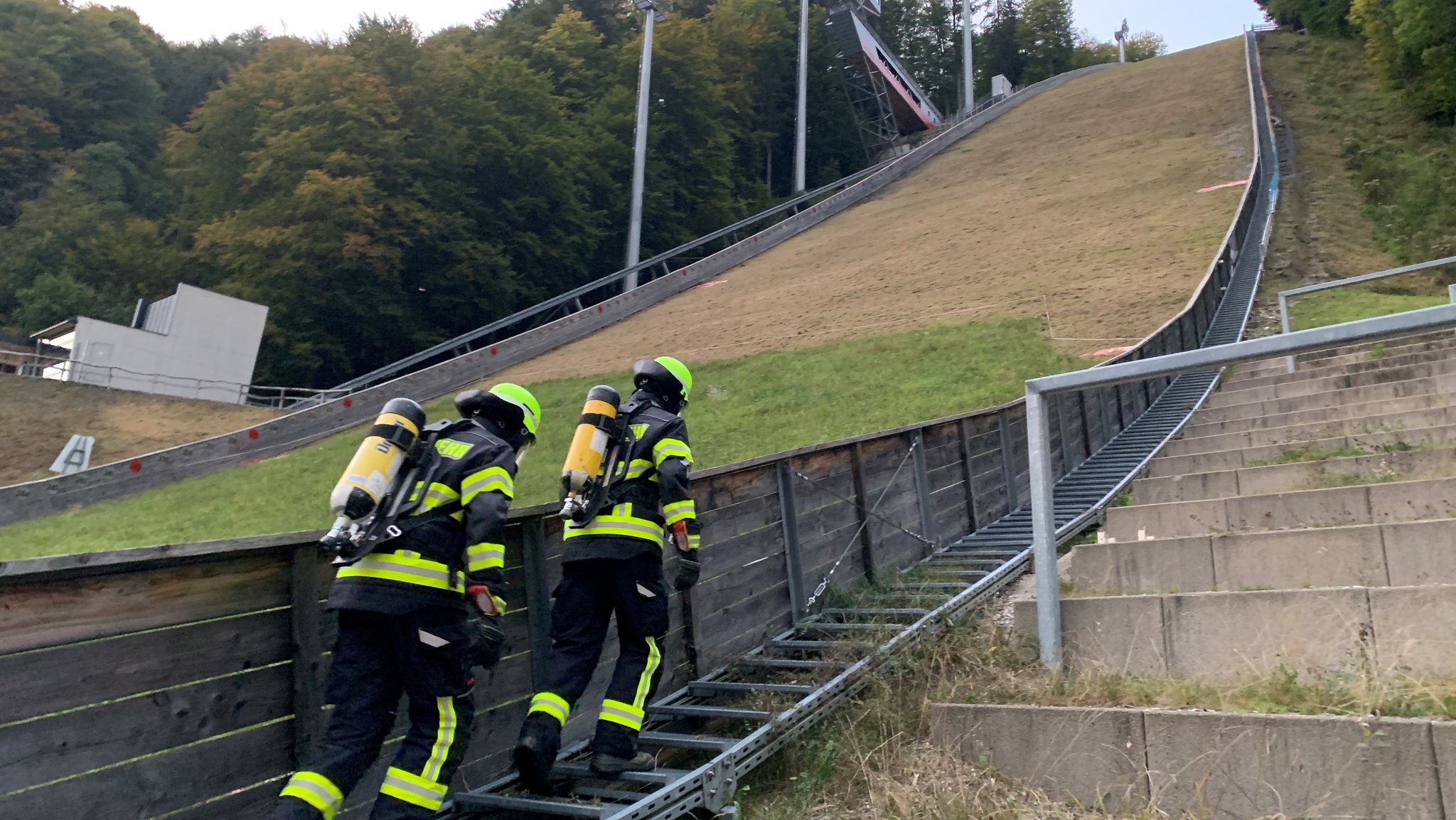 Feuerwehrleute in voller Montur laufen die Heini-Klopfer-Schanze hoch. 