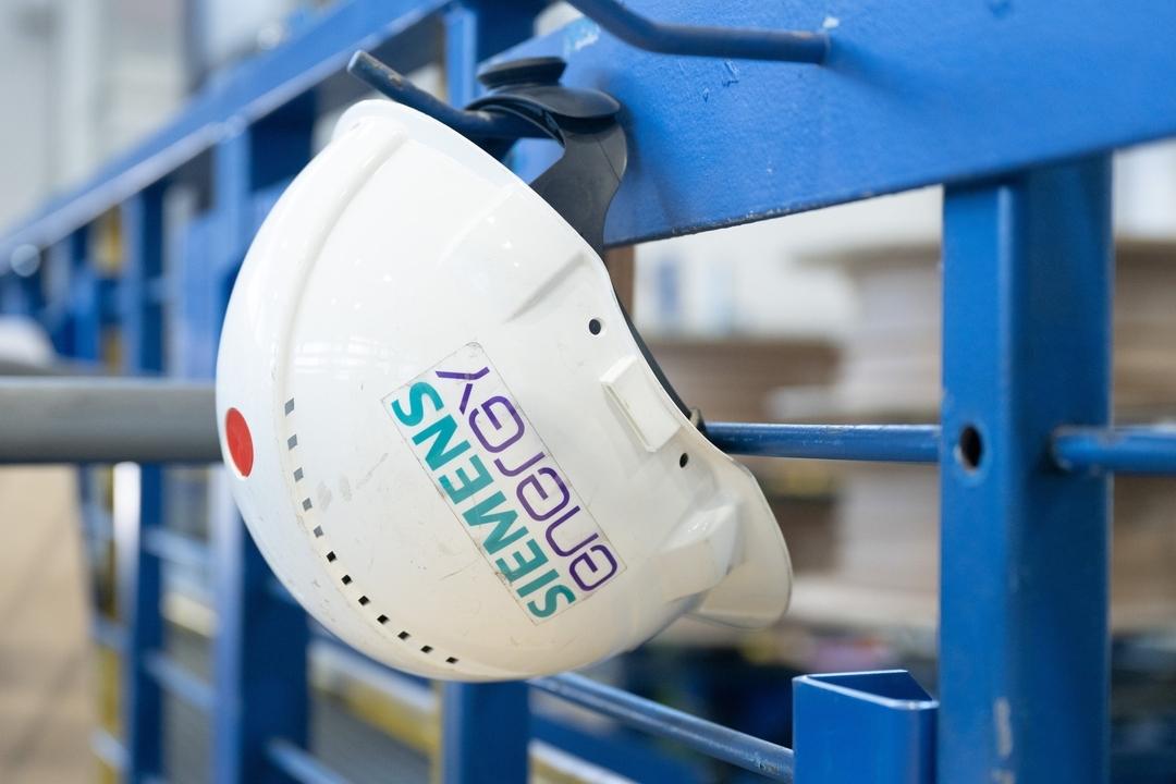Ein Schutzhelm mit der Aufschrift "Siemens Energy" hängt in einer Werkhalle im Transformatorenwerk Siemens Energy.