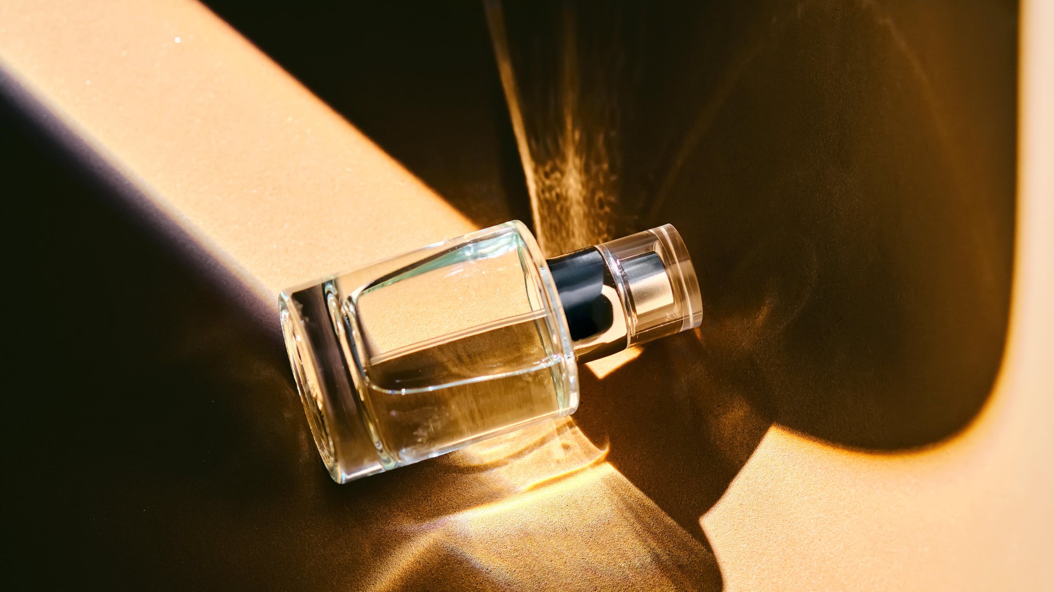 Eine Sprühflasche mit Parfüm liegt auf einem beigen Hintergrund mit einem hellen Lichtstreifen. | Bild: picture alliance / Zoonar | MAREVGENNA Eine Sprühflasche mit Parfüm liegt auf einem beigen Hintergrund mit einem hellen Lichtstreifen.