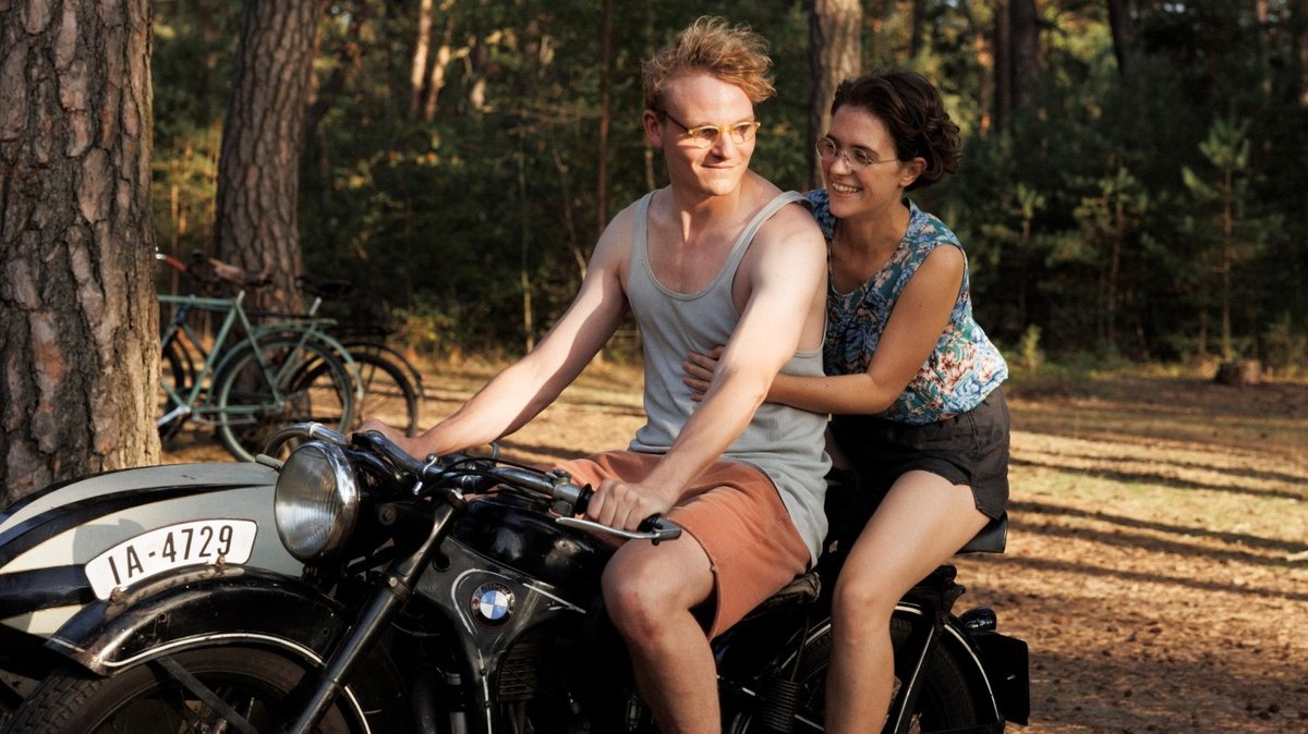 Junger Mann und junge Frau leichtbekleidet und gutgelaunt auf einem altertümlichen Motorrad