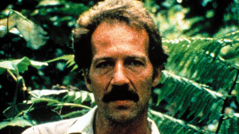  Porträt-Foto von Werner Herzog mit Schnurrbart vor Urwaldhintergrund.