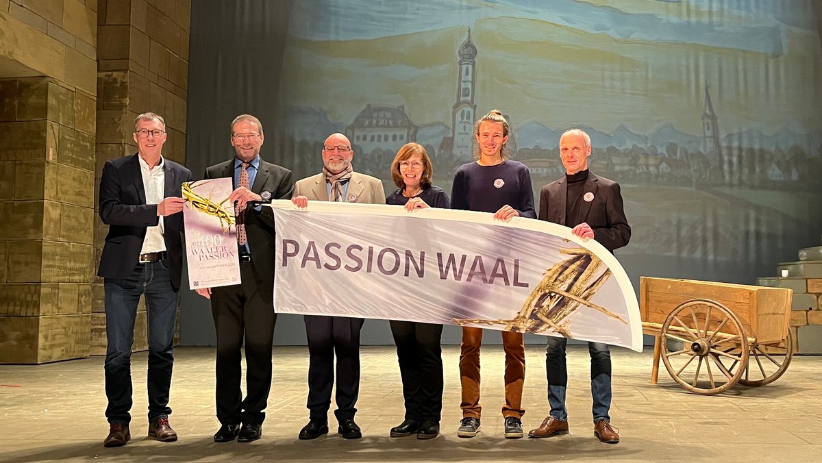 Mitwirkende der Waaler Passion stehen auf der Bühne im Passionsspielhaus und präsentieren das Logo der neuen Waaler Passion.