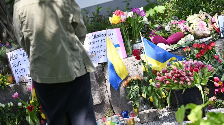 Neben dem Einkaufszentrum, an dem am Samstagabend zwei Männer aus der Ukraine getötet wurden, haben Menschen Blumen und Plakate niedergelegt.  | Bild:dpa-Bildfunk/Angelika Warmuth