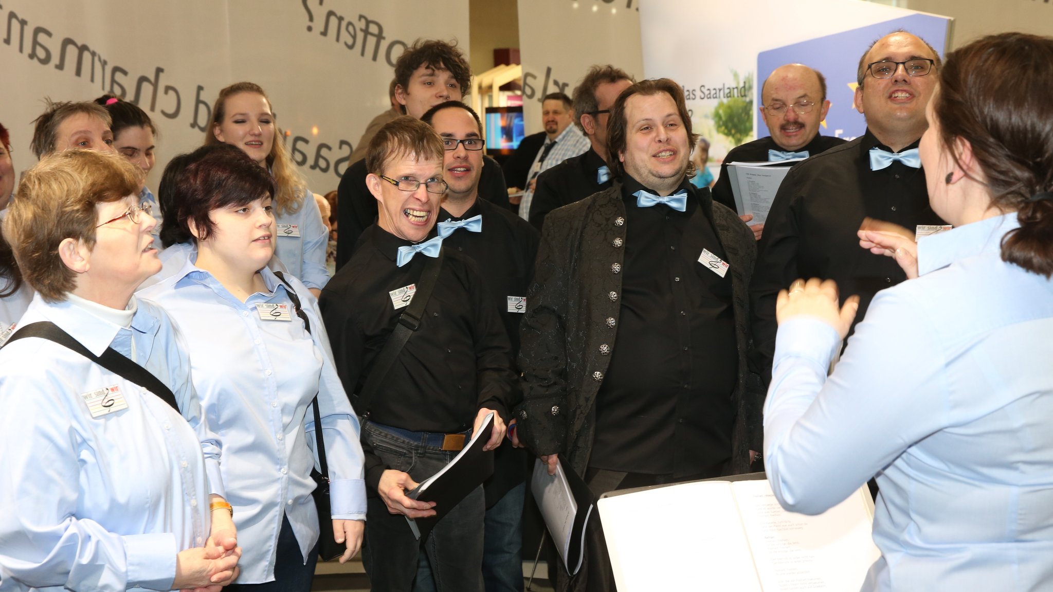 Männer und Frauen singen an einem Messestand.