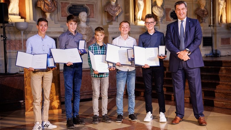 Fünf Jungen, die im Juli eine Frau gerettet haben, stehen mit Urkunden und Medaillen in den Händen neben dem Ministerpräsidenten Markus Söder.