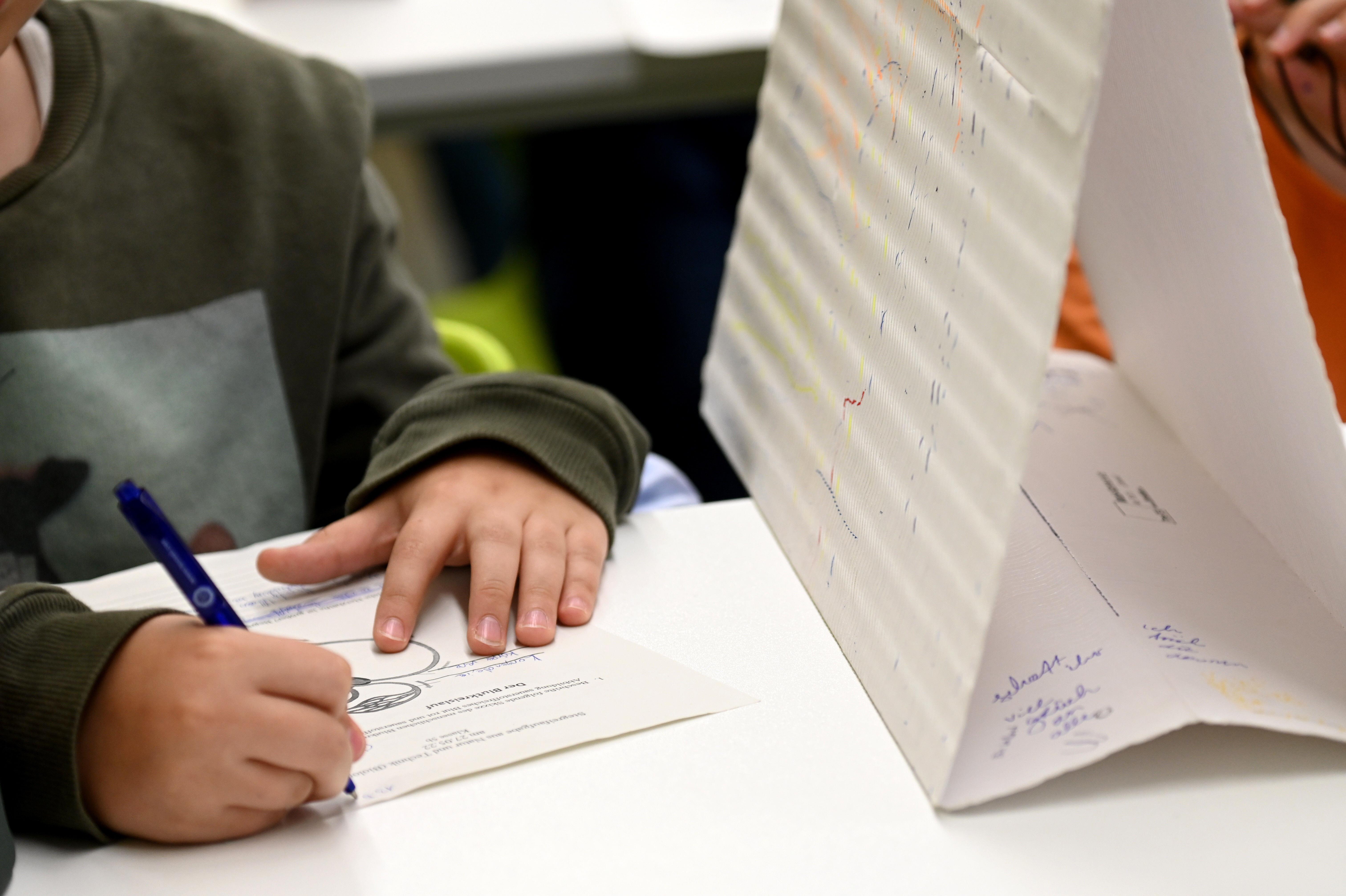 Ein Schüler sitzt an seinem Tisch und schreibt mit einem Schrift auf das Blatt einer Stegreifaufgabe. 