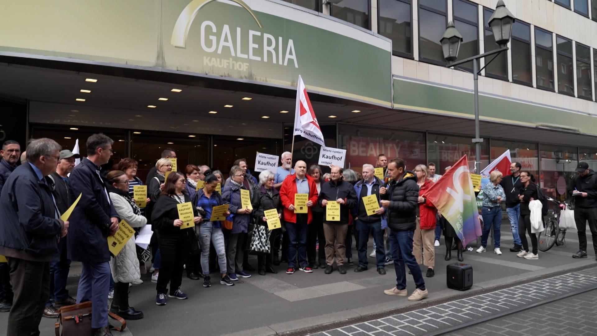 Menschen stehen mit Fahnen und Plakaten vor der Kaufhof Filiale in Würzburg