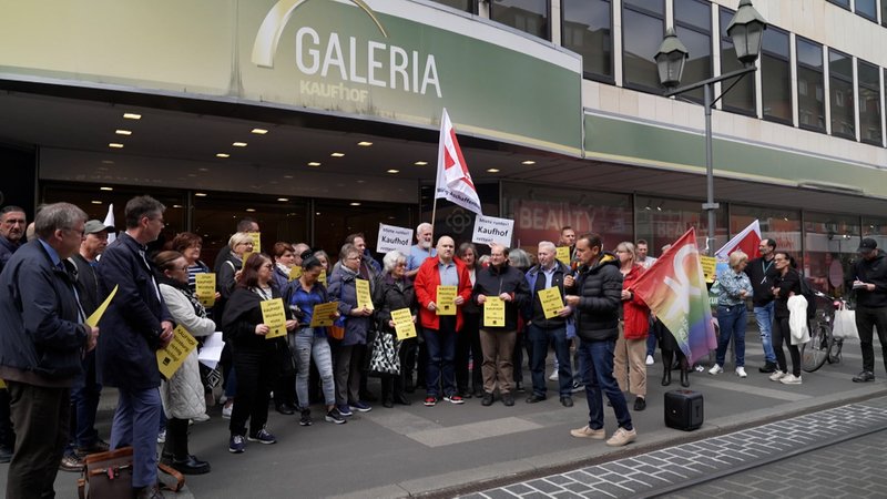 Menschen stehen mit Fahnen und Plakaten vor der Kaufhof Filiale in Würzburg