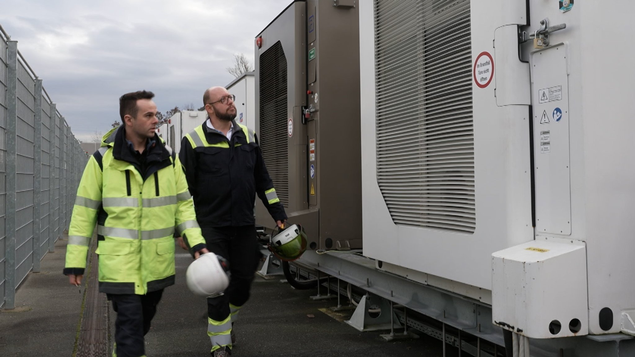 Zwei Mitarbeiter von Fluence auf dem Weg zu einem Batteriespeicher. Diese können Strom aus dem Netz aufnehmen und später wieder abgeben.