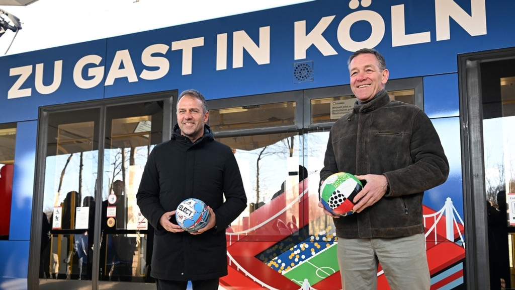 Fußball-Bundestrainer Hansi Flick (links) und Handball-Bundestrainer Alfred Gislason stehen vor einer Straßenbahn. In Köln wurde eine Straßenbahn mit dem Design der Fußball-EM 2024 und der Handball-EM 2024 in Deutschland präsentiert.