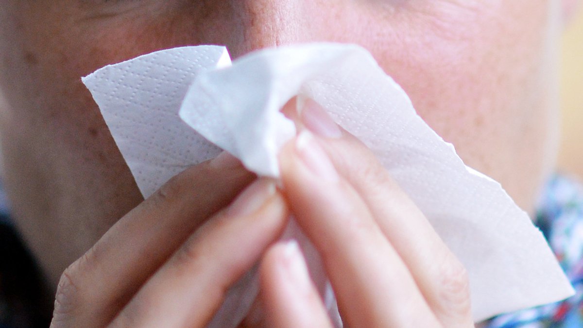 Eine mit einem Atemwegsinfekt erkrankte Frau putzt sich mit einem Taschentuch die Nase. 