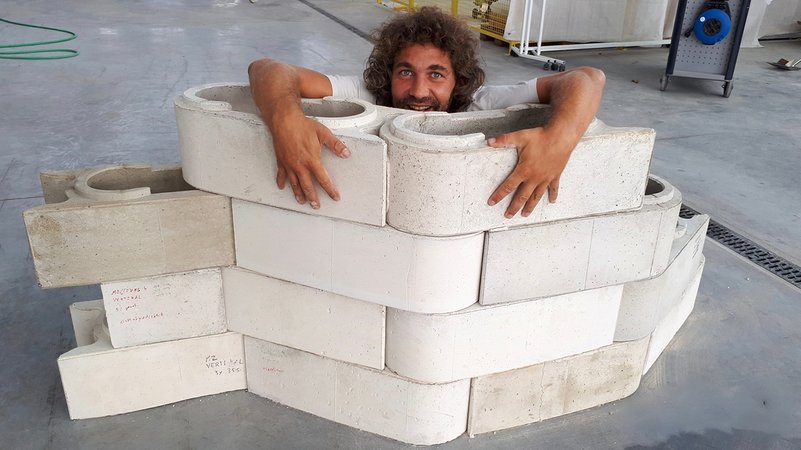 Hinter einer kleinen Mauer aus zusammengesteckten Betonsteinen blickt ein bärtiger Mann hervor und lächelt in die Kamera | Bild: Start Somewhere Hinter einer kleinen Mauer aus zusammengesteckten Betonsteinen blickt ein bärtiger Mann hervor und lächelt in die Kamera