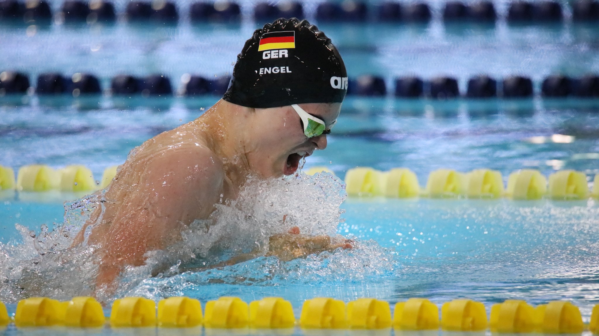 Taliso Engel mit schwarzer Badekappe schwimmt zwischen zwei gelben Absperrungen.