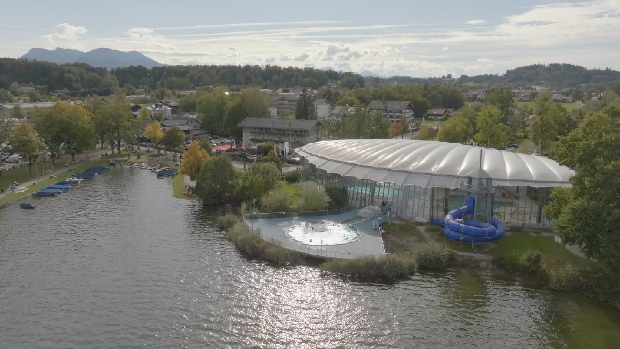 Chiemsee mit Außenbecken, Rutsche und Schwimmbadhalle des Erlebnisbades Prienavera in Prien. 