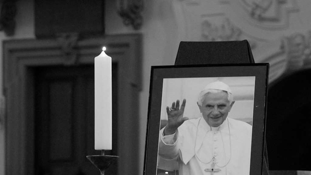 Eine brennende Kerze steht im Würzburger Dom, daneben ein Porträt des verstorbenen Papsts Benedikt.