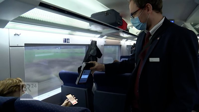 Ein Schaffner und die Zug-Fahrgäste tragen Maske. 
