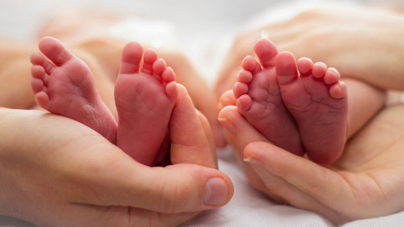 Die Hände von Mutter und Vater umarmen die Füße der Zwillingsbabys auf einem hellen Hintergrund. | Bild: stock.adobe.com/Avril Die Hände von Mutter und Vater umarmen die Füße der Zwillingsbabys auf einem hellen Hintergrund.