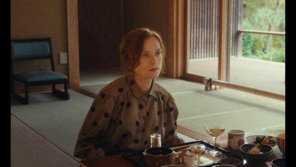 In ihrer Rolle als Schriftstellerin Sidonie Perceval sitzt Isabelle Huppert an einem Tisch mit japanischem Essen und schaut ins Leere.