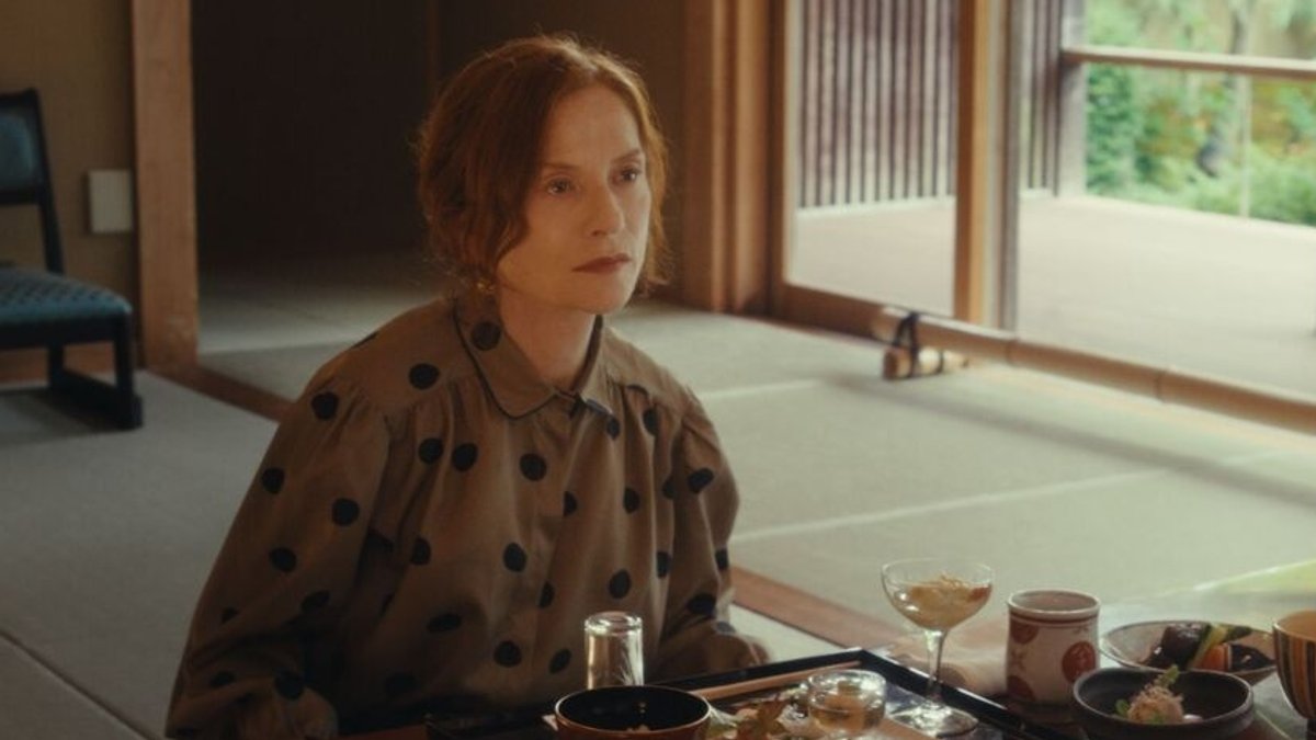 In ihrer Rolle als Schriftstellerin Sidonie Perceval sitzt Isabelle Huppert an einem Tisch mit japanischem Essen und schaut ins Leere.