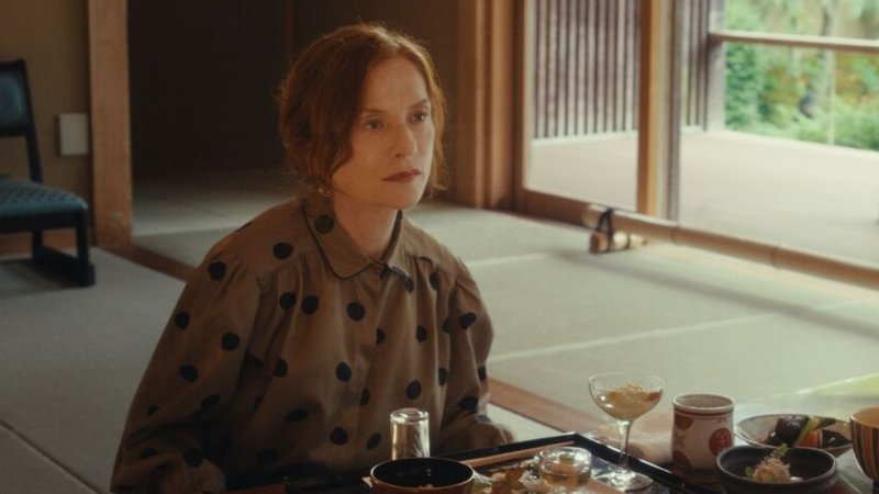 In ihrer Rolle als Schriftstellerin Sidonie Perceval sitzt Isabelle Huppert an einem Tisch mit japanischem Essen und schaut ins Leere. | Bild: Lupa Film In ihrer Rolle als Schriftstellerin Sidonie Perceval sitzt Isabelle Huppert an einem Tisch mit japanischem Essen und schaut ins Leere.