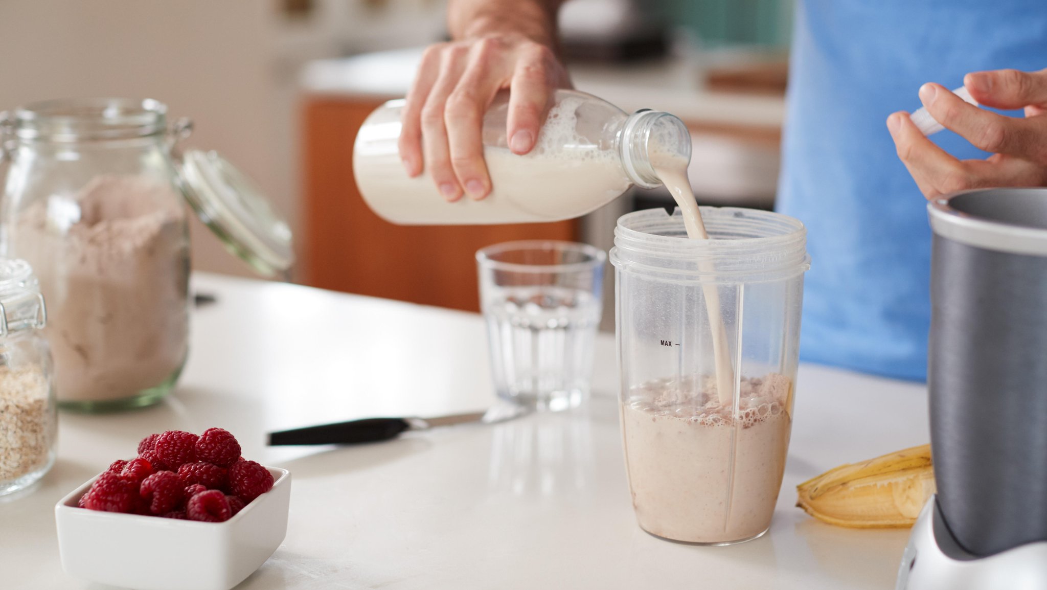 Eine Hand schüttet Milch in einen Mixbecher mit anderen Inhaltsstoffen