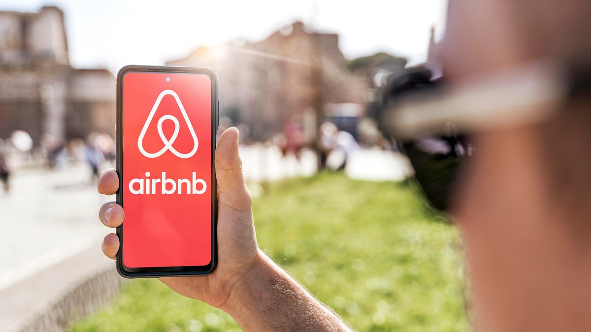 Ein junger Mann hält ein Smartphone mit der Airbnb-App in der Hand und meldet sich für eine einfache und bequeme Hotelbuchung an 