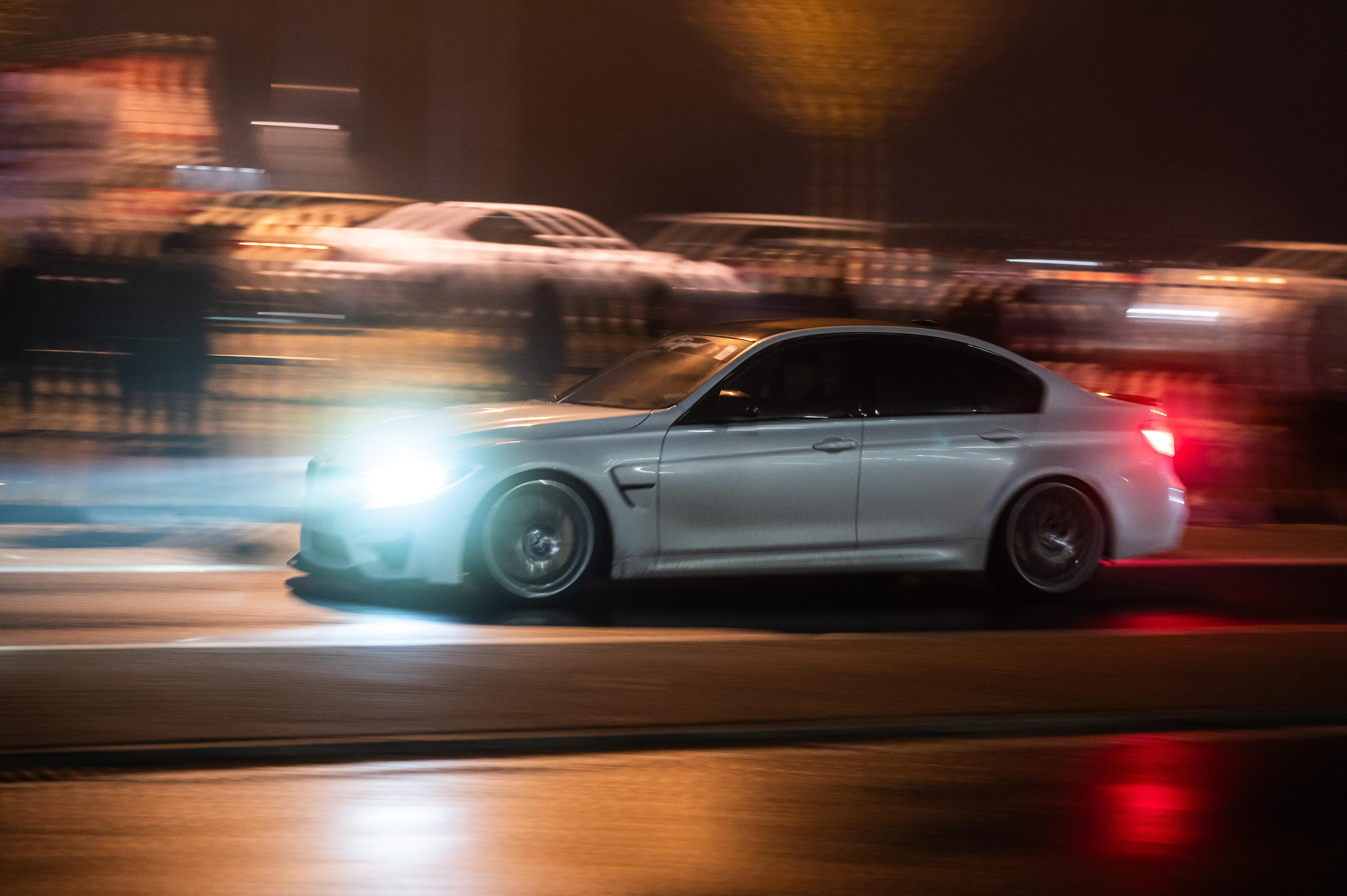 Silbernes Tuning-Auto auf der Straße, Scheinwerfer leuchten, Bild leicht verschwommen.