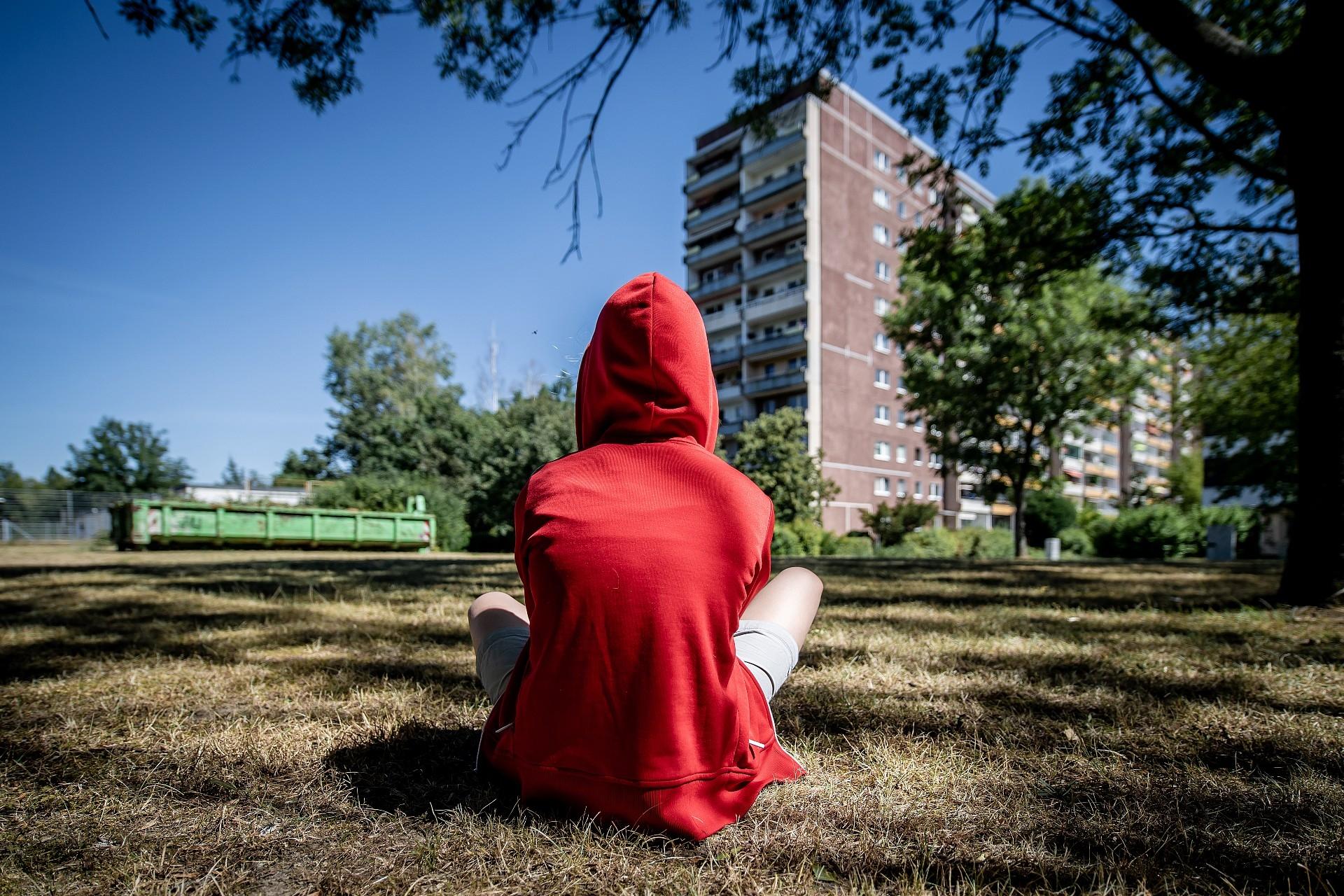 Jugendlicher sitzt im Rasen vor einem Plattenbau