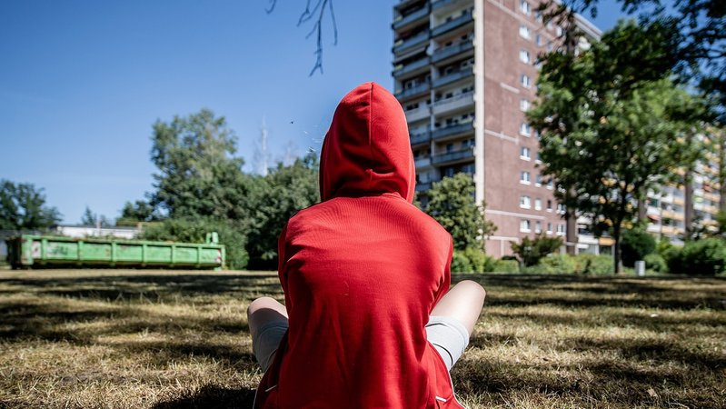 Jugendlicher sitzt im Rasen vor einem Plattenbau | Bild: picture alliance / ZB | Thomas Eisenhuth Jugendlicher sitzt im Rasen vor einem Plattenbau