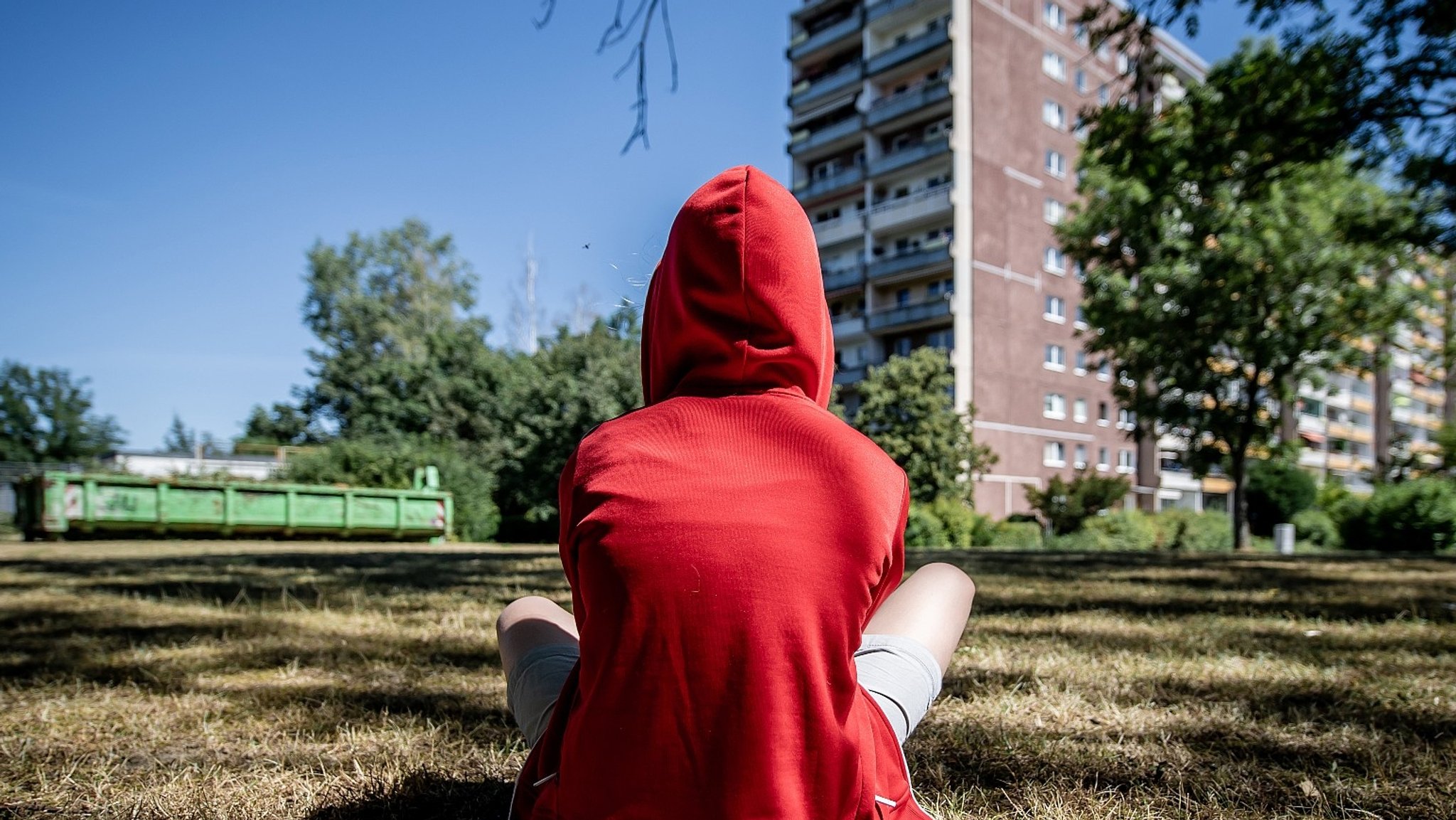 Jugendlicher sitzt im Rasen vor einem Plattenbau