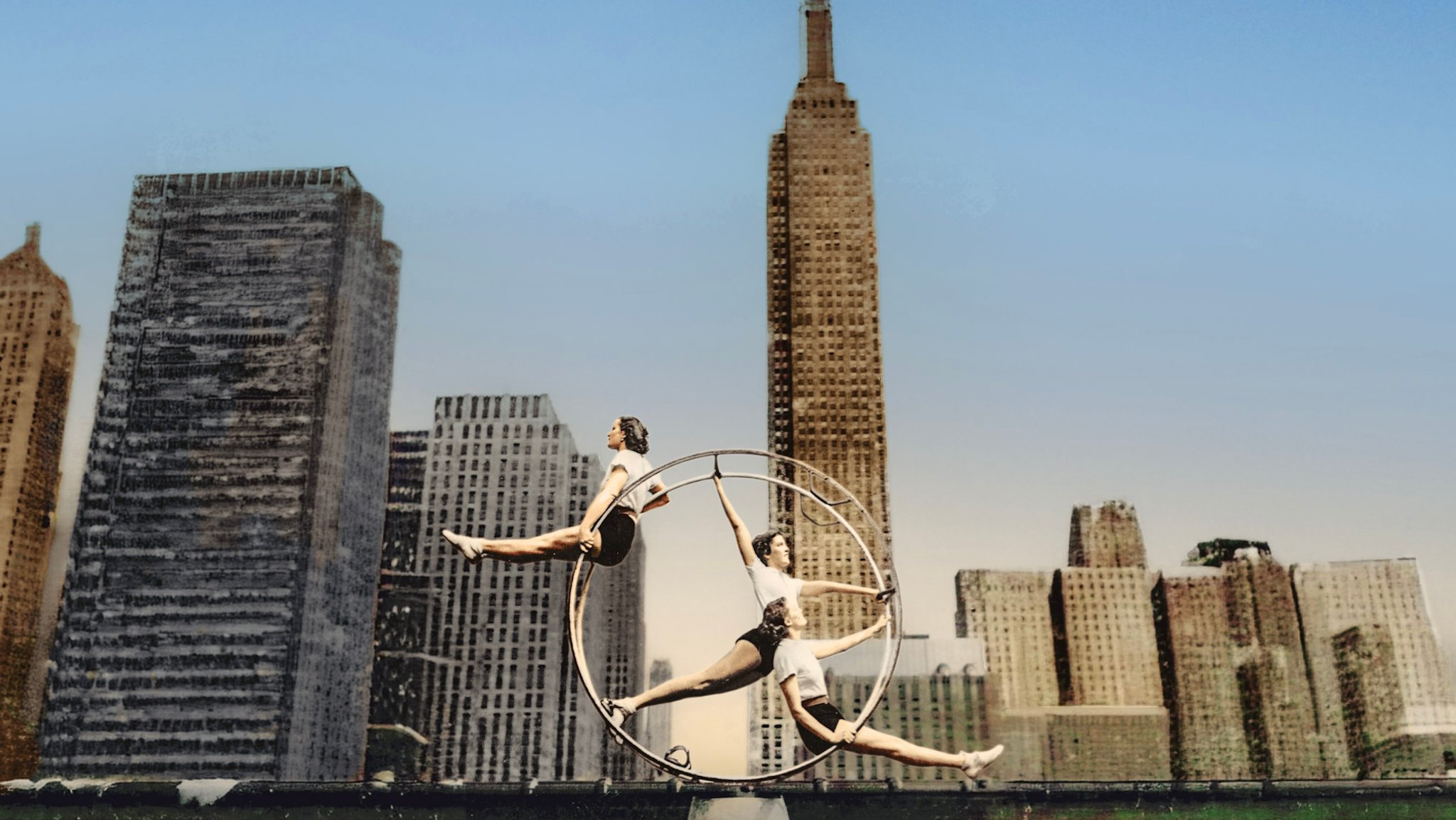 (Archivbild) Drei Turnerinnen in einem Rhön-Rad. Im Hintergrund: die Wolkenkratzer von New York. | Bild: Anita Zirkelbach (zur Verfügung gestellt und bearbeitet von Andreas Brauner) (Archivbild) Drei Turnerinnen in einem Rhön-Rad. Im Hintergrund: die Wolkenkratzer von New York.