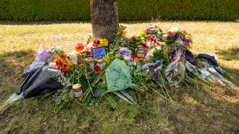 Blumen, Kerzen und Bilder liegen an einem Baum, in dessen Nähe am 17.08.2022 eine weibliche Leiche in einem PKW entdeckt wurde.
