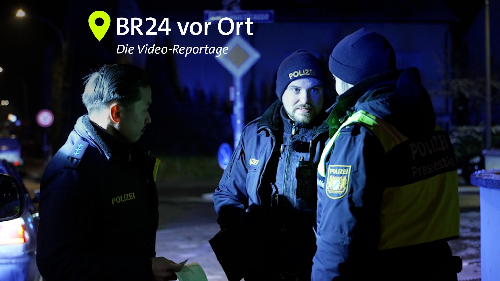 Drei Männer in dunkelblauen Uniformen mit der Aufschrift "Polizei" stehen in der Dunkelheit beieinander.