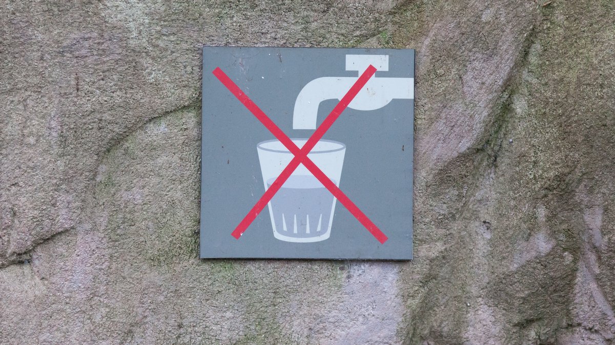 Graues Schild auf grauem Untergrund, auf dem ein Leitungshahn mit einem Glas Wasser zu sehen ist. Beides ist durchgestrichen: Nicht trinken!